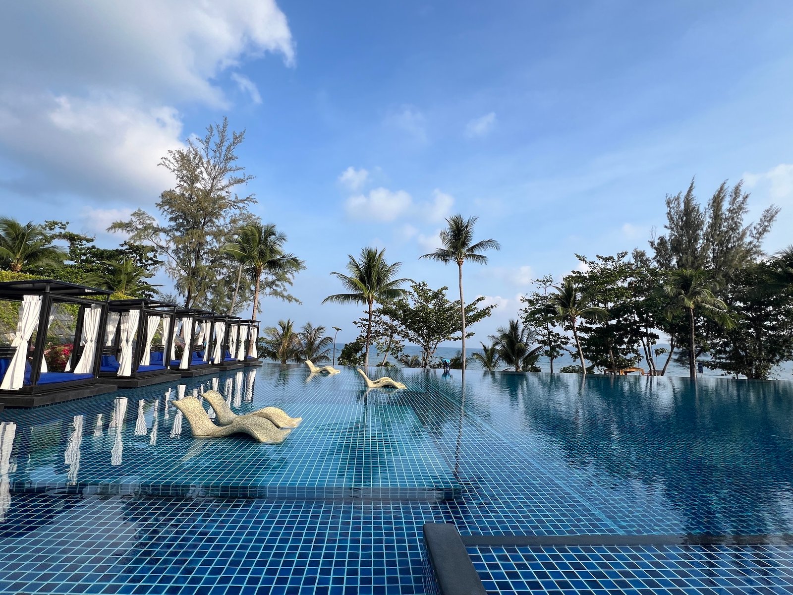 Large hotel pool with cabanas to the left and palm trees ahead