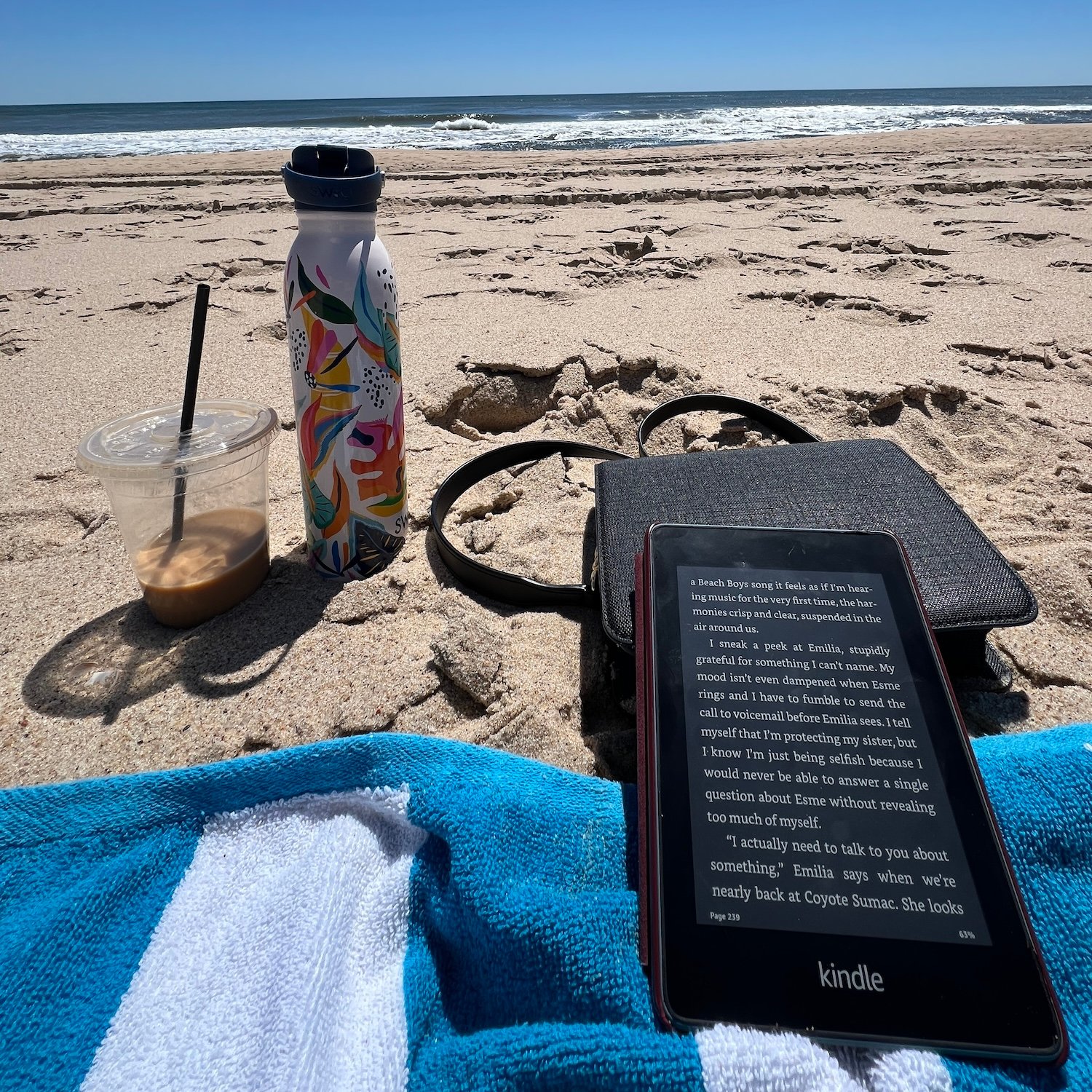 Kindle paperwhite on a beach towel, propped on top of a purse. Waves crashing in the background